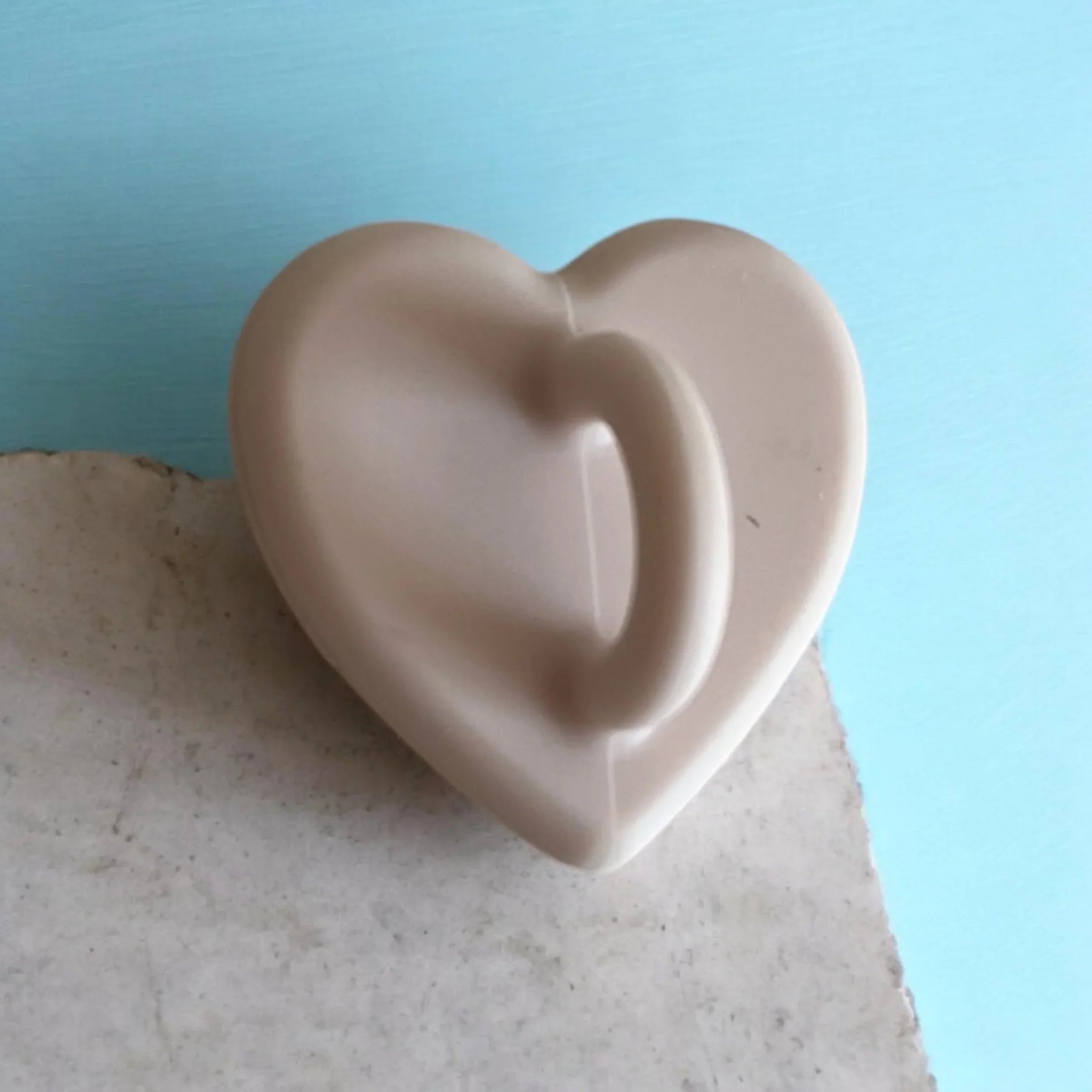 Beige heart-shaped soap dish on stone surface against blue background
