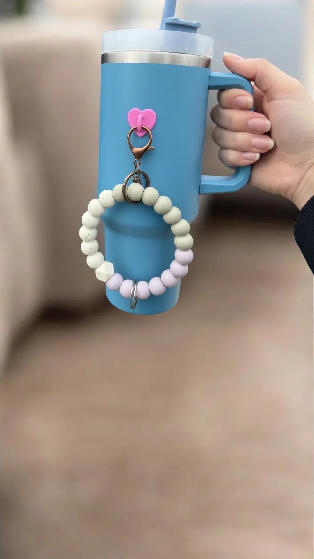 Blue tumbler with pastel beaded strap and pink heart charm, held in hand