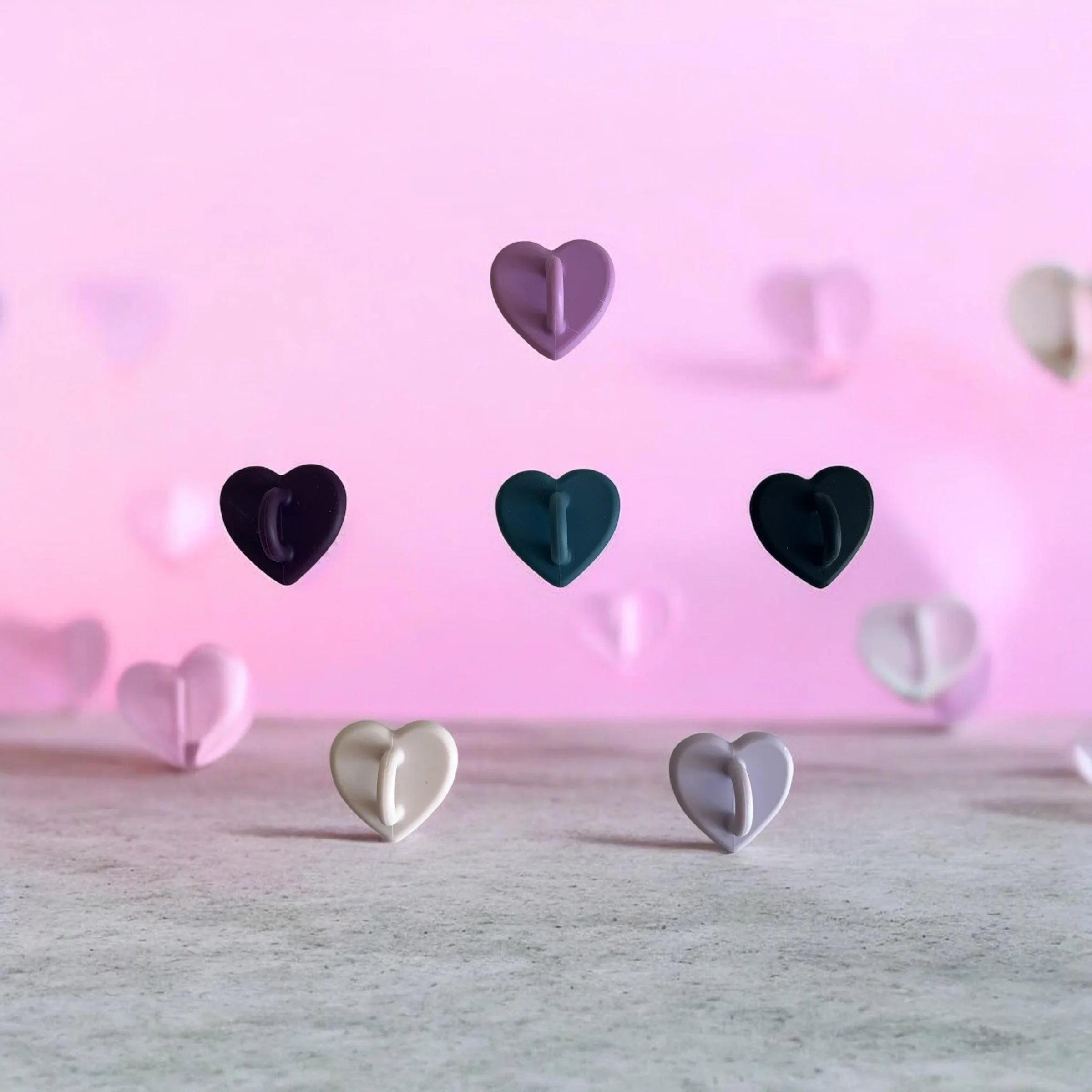 Heart-shaped wall hooks in pastel and dark colors on pink background, perfect for home organization
