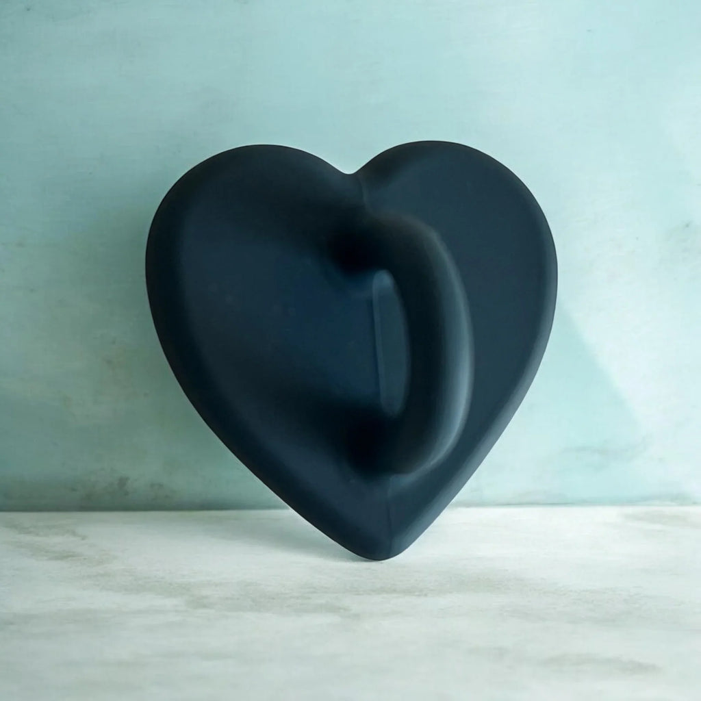 Matte black heart-shaped object with smooth curves against light teal wall