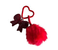 Red heart-shaped keychain with a bow and red pom-pom on a light gray background