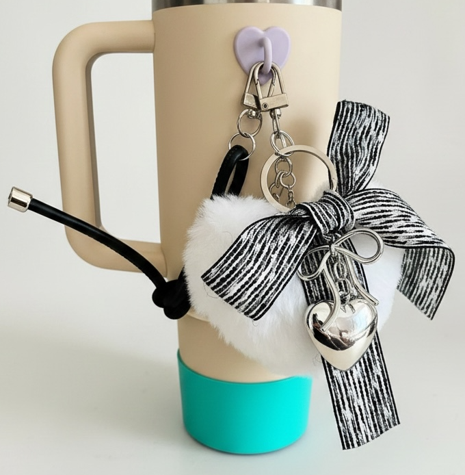 Travel mug with decorative bow, keychain, and charm on a light background