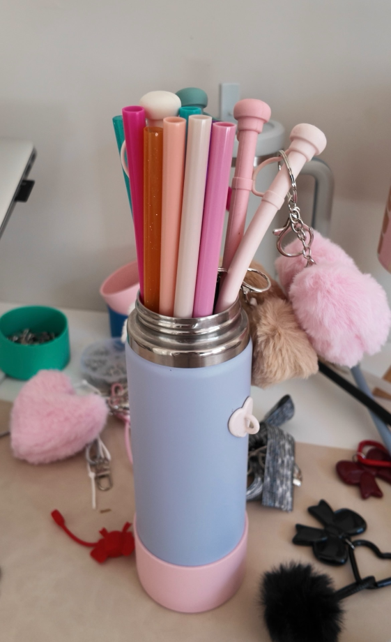 Colorful straws in a pink and blue holder on a desk with various items.